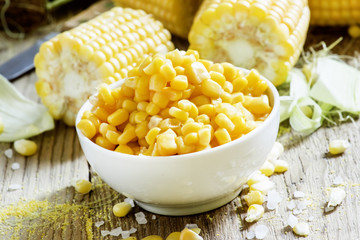 Canned sweet corn in white bowl, fresh cobs, wood background, se