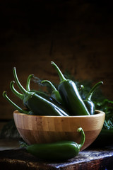 Green burning mexican jalapeno pepper in bowl, vintage dark wood