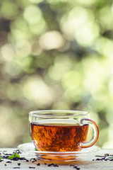 Cup of black tea on the open window on green blurred nature back