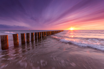 Baltic sea coast on colorful sunset with wooden groyne, Poland