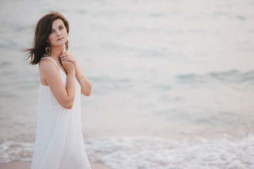 Fototapeta na wymiar Young beautiful woman in a white dress walking on an empty beach near ocean