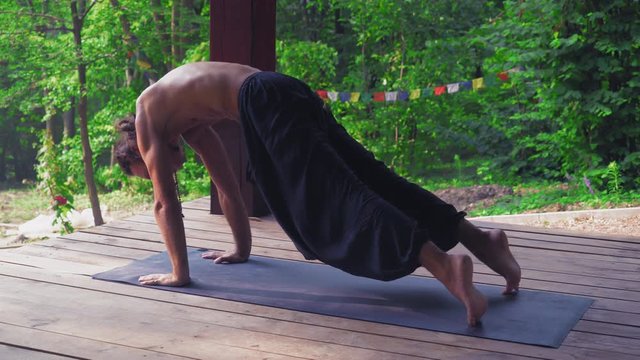 A Man In Dark Pants Outdoors In A Park On The Mat Performing Yoga Exercises.