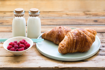 Delicious breakfast with fresh croissants, raspberries and milk on old wooden background