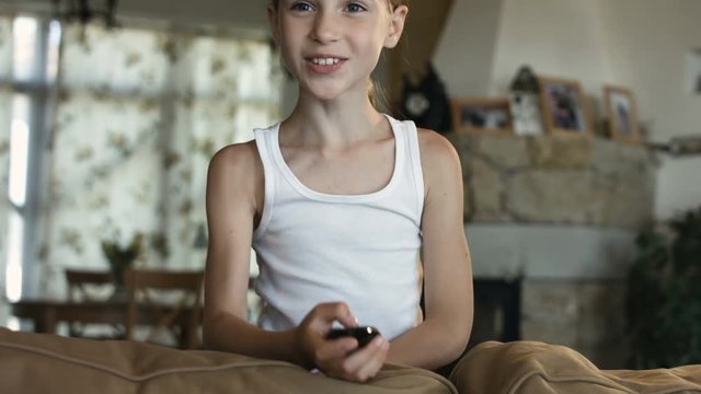 Child watching TV, little girl having fun on the couch, holding remote control