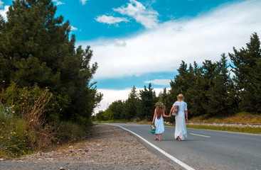 mother and daughter are walking on road both are barefeet and wear white dresses