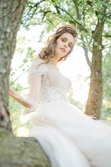 Naklejka premium Young bride in beautiful wedding dress sitting on tree outdoors