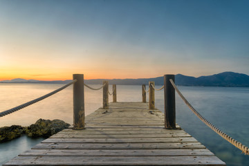 Fototapeta premium Wooden bridge against the sunset and sea at Oropos in Greece. 