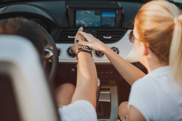 cheerful family couple lovers smiling and cheating to each other driving a cabriolet and searching the location they need by pointing on car gps system