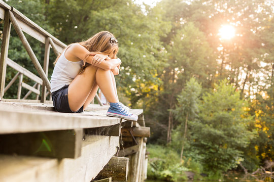 Young woman resting on a wooden bridge in jeans sneakers