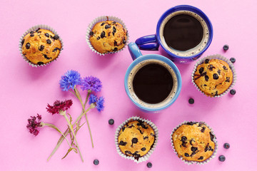 Blueberry muffins, two cups of coffee and cornflowers on pink ba