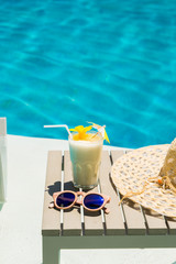 Swimming pool table with sunglasses, hat and fresh cocktail