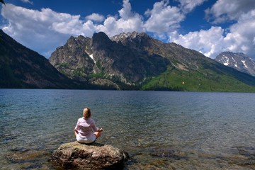 Fit woman in yoga pose meditating in nature. Jenny Lake in Grand Tetons National Park, Jackson, Wyoming, USA. 