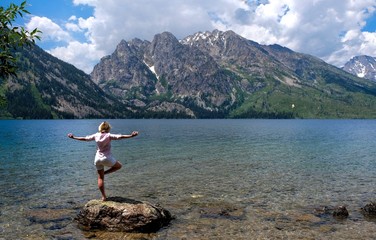 Fit woman in yoga pose meditating in nature. Jenny Lake in Grand Tetons National Park, Jackson, Wyoming, USA. 