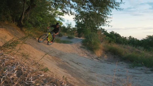 A mountain biker riding and jumping on track downhill at sunrise, slow motion