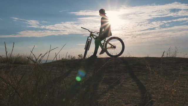 A mountain biker sitting on his bike at sunrise or sunset near the sea, dolly