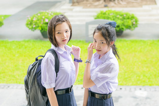     Cute Asian Thai high schoolgirls student couple in school uniform standing with her friend showing curious or watching face expression 