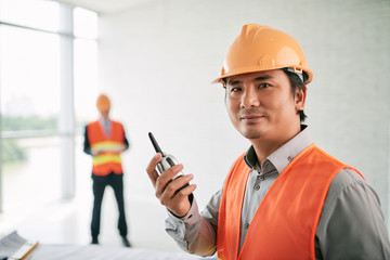 Portrait of smiling Vietnamese contractor with walkie-talkie in his hands
