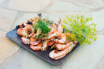 Tasty giant shrimps langoustines grilled on barbecue placed on plate with greens
