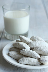 the cookies with powdered sugar in a plate and a glass of milk on wooden background.Monochrome