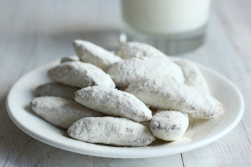 the cookies with powdered sugar in a plate and a glass of milk on wooden background.Monochrome