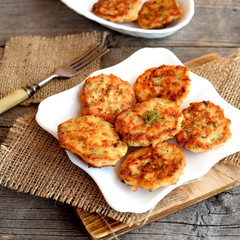 Fried cutlets of minced fish on the plate. Fork, cutting board, burlap on wooden background. Delicious and healthy salmon recipe