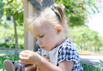 Cute little girl with straight face in summer day. mending sandals.