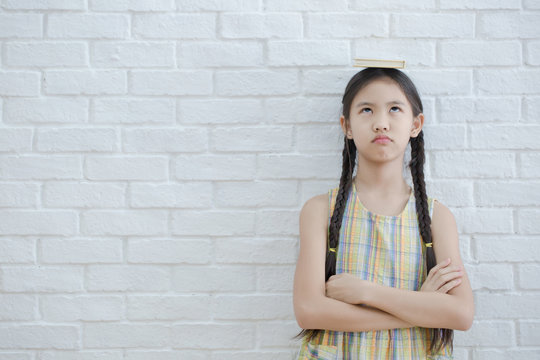 Funny action portrait of Asian girl reading story book on white brick wall