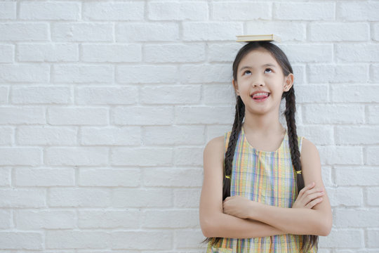 Funny action portrait of Asian girl reading story book on white brick wall