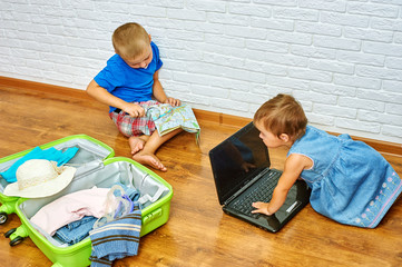 brother and sister sitting on the floor near the suitcase, studying a map and looking at laptop