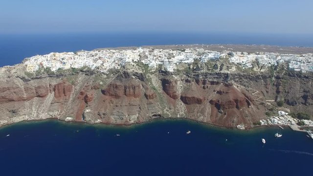 Aerial footage of Oia, Santorini - Famous white houses and blue domes on the edge of the cliff and blue lagoon.