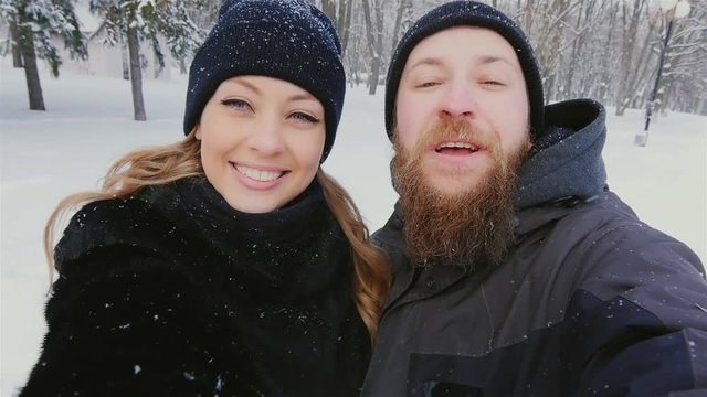 Funny woman and a bearded man doing selfie winter in snow, falling snowflakes