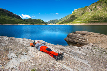 Man rests and sleeps near a mountain lake during an alpine hikin