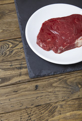 A cut of raw rump steak meat on a reclaimed wooden table top background forming a page border