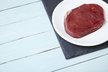 A uncooked fillet of steak meat on a painted wooden table background forming a page border
