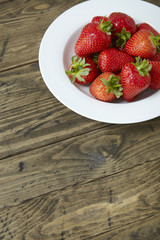 A bowl of fresh home grown strawberries on a rustic table top background forming a page border