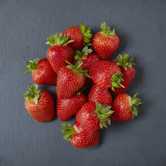 An aerial view of a pile of whole ripe strawberries on a rustic slate background