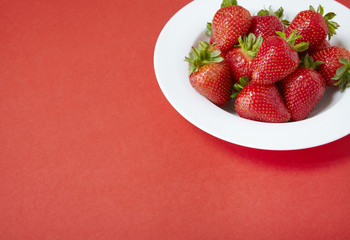 A bowl of whole ripe strawberries on a red background forming a page border