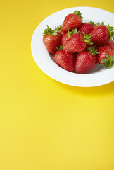 A bowl of whole ripe strawberries on a yellow background forming a page border