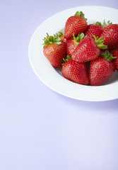 A bowl of fresh ripe strawberries on a purple background forming a page border
