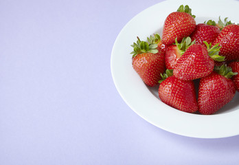 A bowl of whole ripe strawberries on a purple background forming a page border