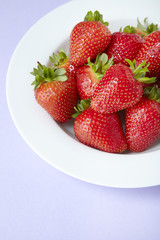 A bowl of whole ripe strawberries on a purple background