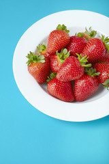 A bowl of fresh ripe strawberries on a blue background