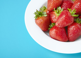 A bowl of whole ripe strawberries on a bright blue background