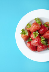 An aerial view of a bowl of whole ripe strawberries on a blue background
