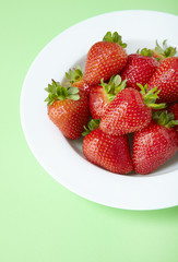 A bowl of fresh ripe strawberries on a pastel green background