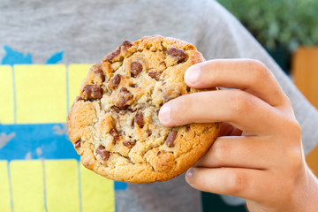 Child holding large homemade chocolate chip cookie.