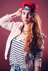 Sexy hip-hop woman in cap with long red hair. Fashion portrait of modern girl in cap