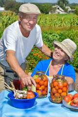 женщина с мужчиной летом на огороде консервируют овощи