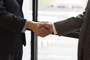 businessmen in suit shaking hands beside window - business teamw