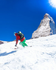 Skier skiing downhill in high mountains against sunshine